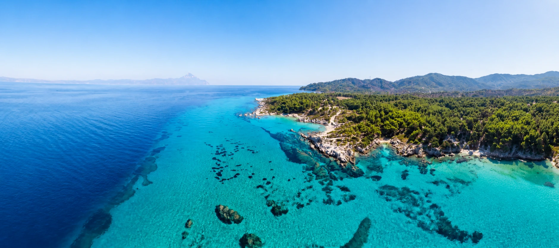 Aerial view of a clear blue coastline and a forested peninsula.